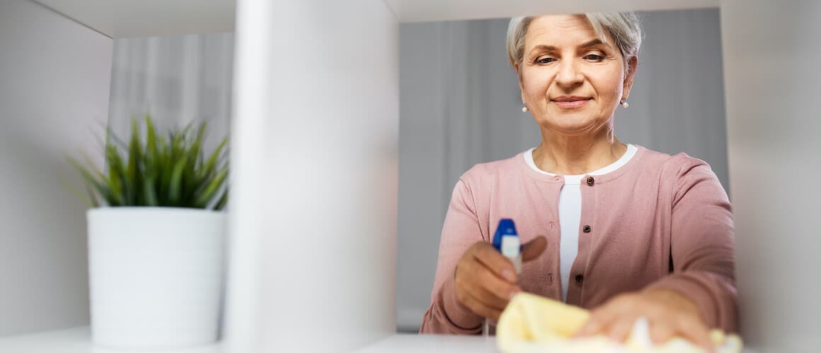 Senior woman cleaning a shelf in her home.