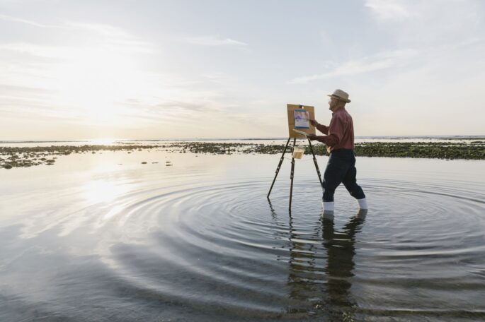 senior man painting a picture while standing in water
