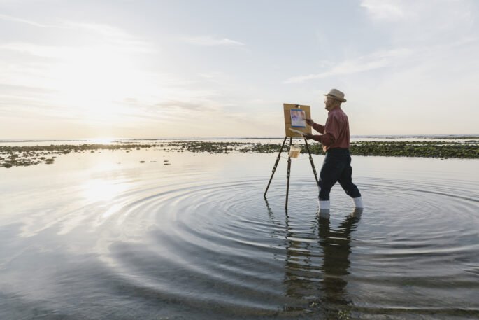 senior man painting a picture while standing in a shallow pond